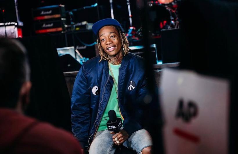 A musician in a blue bomber jacket mid-interview on a television set.