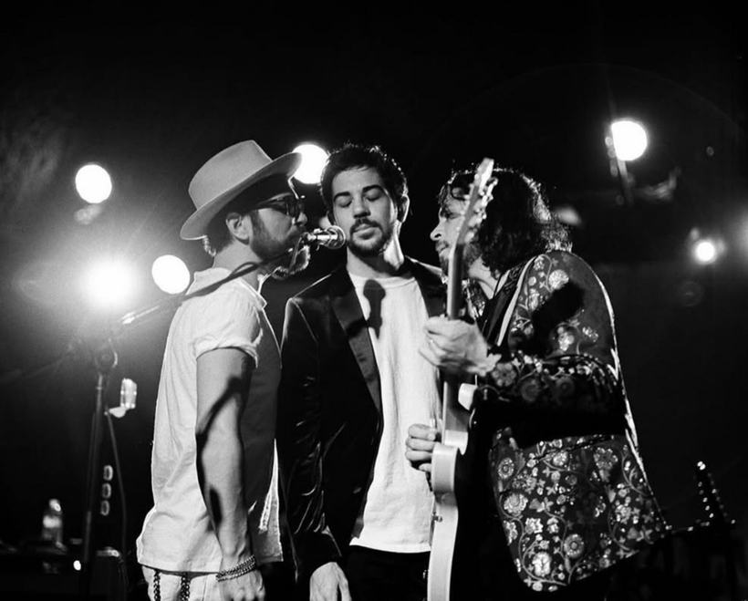 A black and white photo of a band sharing a laugh under stage lights.