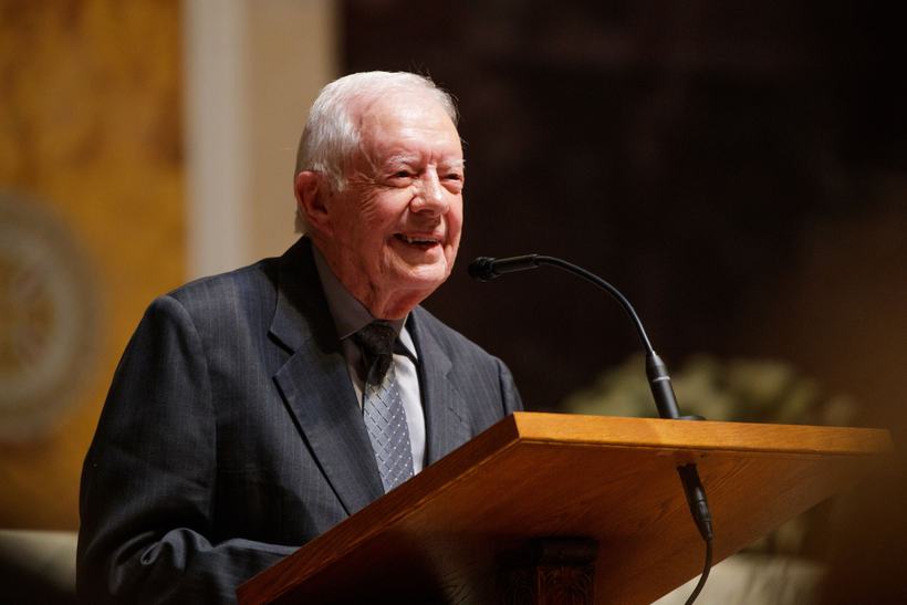 Former President Jimmy Carter smiling at a wooden podium.