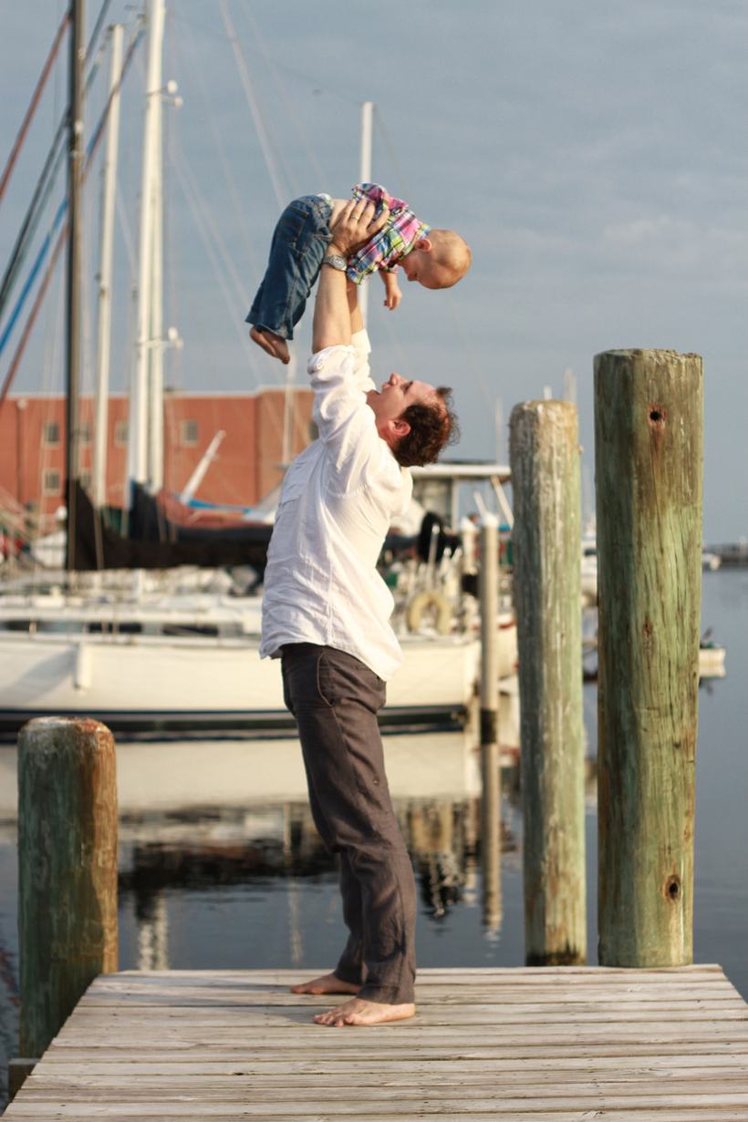 A father lifting his child into the air on a marina dock.