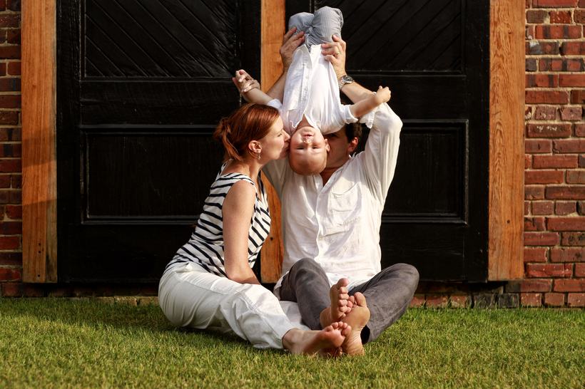 Parents playing with their young children on the grass by a barn door.