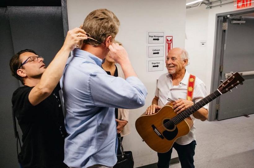 A guest being fitted with a microphone backstage beside a guitarist.