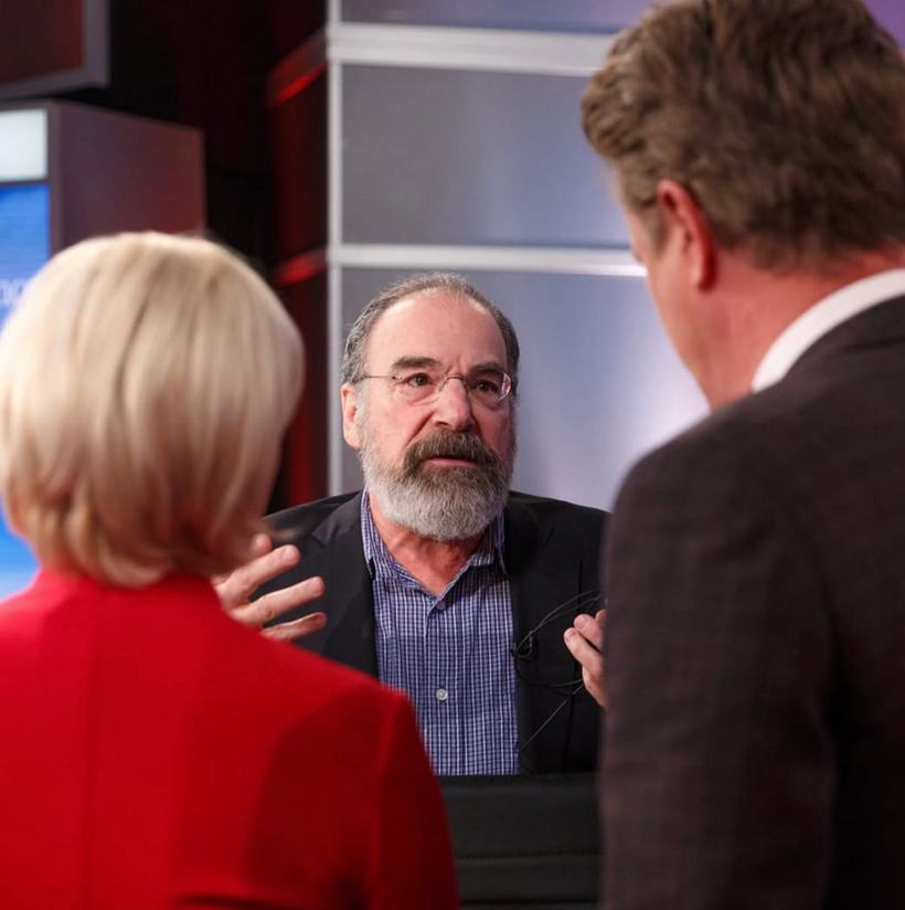 A bearded guest in conversation with two hosts on set.