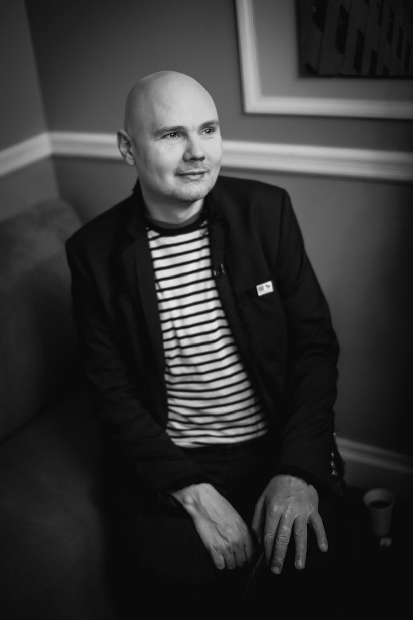 A black and white portrait of a seated man in a striped shirt.