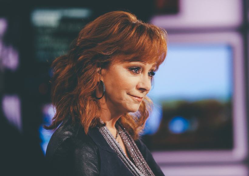 A red-haired woman in a leather jacket on a television set.