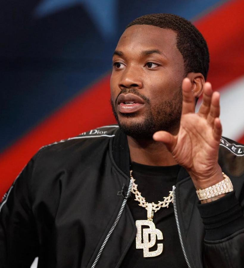A man in a black jacket and chain gesturing mid-interview.