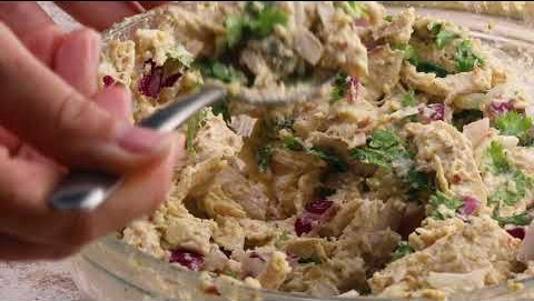 A fork folding herbs into an enchilada filling in a glass bowl.