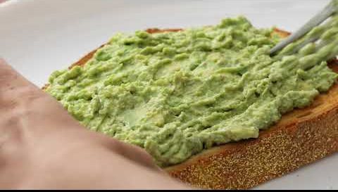 A fork spreading a bright green dip across thick toast.